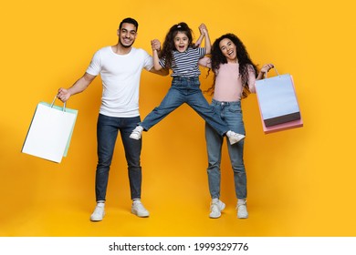 Portrait Of Excited Arab Parents And Little Daughter Holding Bright Shopping Bags And Having Fun Together Over Yellow Studio Background, Middle Eastern Family Enjoying Seasonal Shopping, Free Space