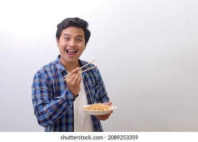 Portrait of excited Asian man in blue plaid shirt eating instant noodles while raising his chopsticks up and pointing. Isolated image on white background - Powered by Shutterstock