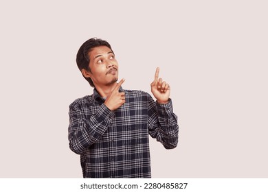 Portrait of excited Asian man in blue checkered shirt smiling and looking sideways pointing with two hands and fingers to the sides. Isolated image on cream background - Shutterstock ID 2280485827