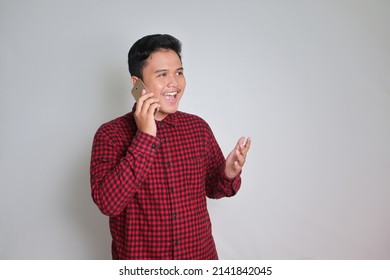 Portrait Of Excited Asian Man In Casual Plaid Shirt Making Phone Call With Explaining Hand Gesture. Isolated Image On Gray Background