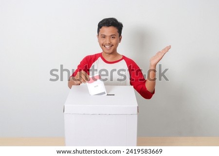Portrait of excited Asian man inserting and putting the voting paper into the ballot box. General elections or Pemilu for the president and government of Indonesia. Isolated image on white background