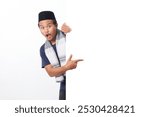 Portrait of excited Asian muslim man wearing sarung scarf hiding behind empty white billboard with mockup template and copy space for graphic. Advertising poster. Isolated on white background