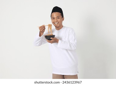 Portrait of excited Asian muslim man eating delicious instant noodles with chopsticks served on plate. Pre dawn meal and break fasting concept. Isolated image on white background