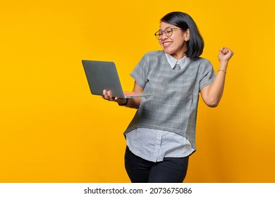 Portrait Of Excited Asian Woman Holding Laptop Over Yellow Background