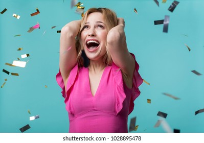 Portrait of excited beautiful woman in cute dress holding her hands on head while looking at golden confetti flying around. Isolated on blue background - Shutterstock ID 1028895478