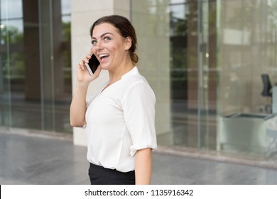 Portrait of excited businesswoman talking on smartphone outdoors. Mid adult Caucasian woman calling client or colleague. Business communication concept - Shutterstock ID 1135916342