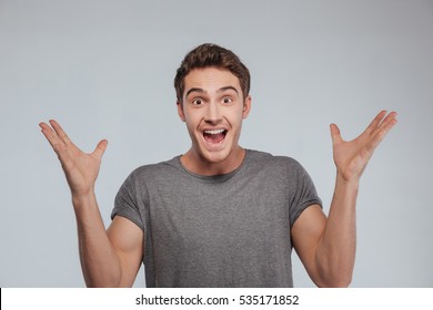 Portrait of an excited casual man standing with raised hands and looking at camera isolated on a white background
