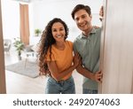 Portrait of excited cheerful couple inviting guest friends to enter their home, happy young guy and lady standing in doorway of contemporary flat, millennial family holding door looking out together