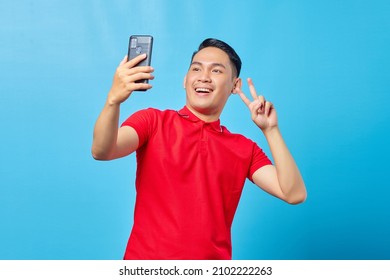 Portrait Of Excited Cheerful Young Asian Man Using Mobile Phone Take Selfie Over Blue Background