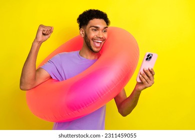 Portrait of excited crazy guy hold inflatable circle buoy raise fist success use smart phone isolated on yellow color background - Shutterstock ID 2311459055