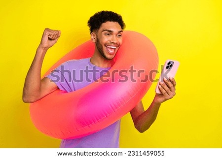 Portrait of excited crazy guy hold inflatable circle buoy raise fist success use smart phone isolated on yellow color background