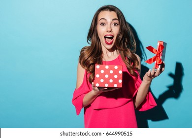 Portrait Of An Excited Cute Girl In Dress Holding Opened Present Box Isolated Over Blue Background