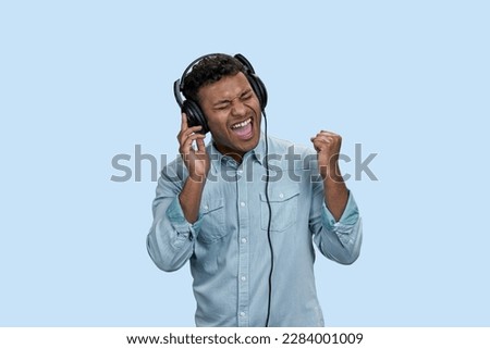 Portrait of excited emotional Indian man listen to music in headphones. Isolated on pastel blue background.