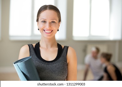 Portrait of excited female yoga teacher posing with fitness mat looking at camera, happy toned fitness instructor or coach in sportswear smiling making picture during training in yoga studio - Powered by Shutterstock