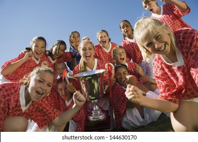 Portrait of excited girls' soccer team holding trophy against clear sky