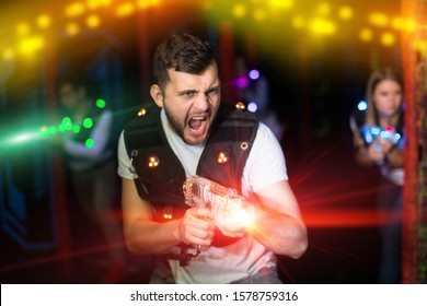 Portrait of excited guy laser tag player with laser pistol in room with bright beams 