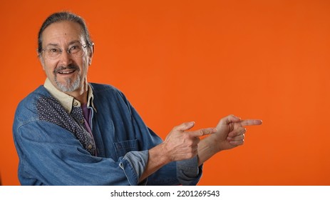 Portrait Of Excited Happy Mature Man 50s Point Finger Aside On Workspace Copy Space Mockup Promo Commercial Area Isolated On Solid Orange Background Studio.