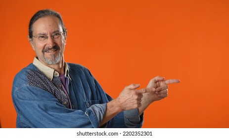 Portrait Of Excited Happy Mature Man 50s Point Finger Aside On Workspace Copy Space Mockup Promo Commercial Area Isolated On Solid Orange Background Studio.