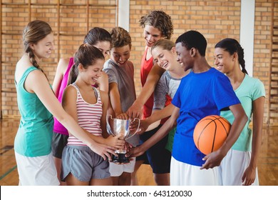 Portrait Of Excited High School Kids Holding Trophy In Basketball Court