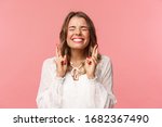 Portrait of excited hopeful blond girl making wish crossed fingers for good luck, close eyes and smiling putting all effort into pray, pleading for dream come true, anticipating over pink background