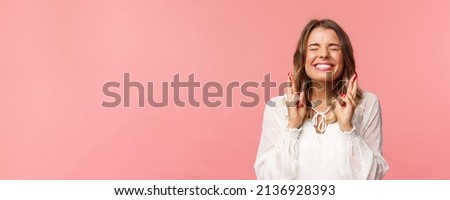 Portrait of excited hopeful blond girl making wish crossed fingers for good luck, close eyes and smiling putting all effort into pray, pleading for dream come true, anticipating over pink background