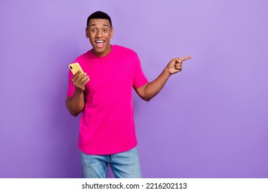 Portrait Of Excited Impressed Man Fade Haircut Wear Pink T-shirt Hold Phone Indicating Empty Space Isolated On Purple Color Background