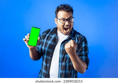 portrait of an excited Indian Caucasian man cheering and showing smart phone with blank green screen isolated on single color background - Powered by Shutterstock