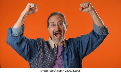 Portrait Of Excited Jubilant Overjoyed Elderly Bearded Man 50s 60s Doing Winner Gesture Celebrate Clenching Fists Say Yes Isolated On Solid Orange Background Studio