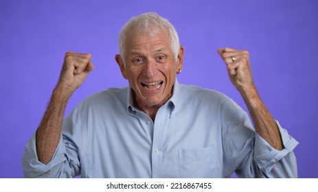 Portrait Of Excited Jubilant Overjoyed Elderly Man 70s Doing Winner Gesture Celebrate Clenching Fists Say WOW Isolated On Solid Purple Background Studio