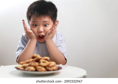 Portrait Of An Excited Little Asian Boy With A Big Stack Of Chocolate Chip Cookies, Wide Eyes And A Huge Smile As He Smells The Delicious Cookies