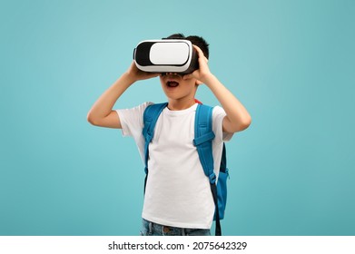 Portrait Of Excited Little Asian Schoolboy Experiencing Virtual Reality In VR Glasses Headset While Standing Over Blue Background In Studio, Korean Kid Enjoying Modern Technologies For Entertainment