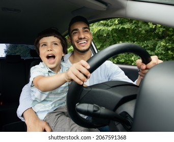 Portrait Of Excited Little Boy Driving Car With His Arab Dad, Holding Steering Wheel And Laughing, Caring Middle Eastern Father Teaching Son How To Drive, Enjoying Road Trip In Modern Vehicle