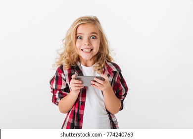 Portrait of an excited little girl holding mobile phone and looking at camera isolated over white background - Powered by Shutterstock