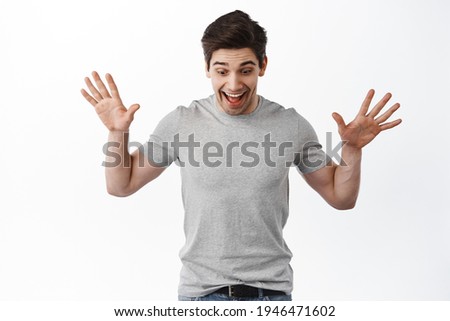 Portrait of excited man raise hands and look amazed down, found something on floor, standing happy against white background