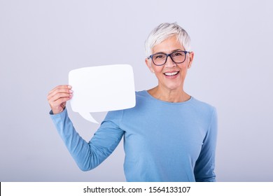 Portrait Of A An Excited Mature Gray Hair Woman Showing Blank Speech Bubble Isolated Over Gray Background. Senior Woman Holding Speech Bubble Banner