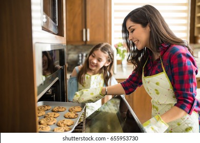 Portrait of excited mom and daughter taking freshly bakes cookies out of the oven