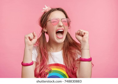 Portrait of excited overjoyed female model clenches fists with pleasure, screams in happiness, celebrates her victory, has great triumph. Fashionable woman gestures joyfully indoors. Success concept