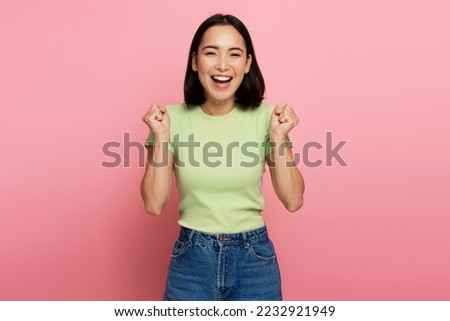 Portrait of excited overjoyed woman standing with raised fists and shouting yeah, I'm winner, rejoicing victory, success. Studio shot isolated on pink background 
