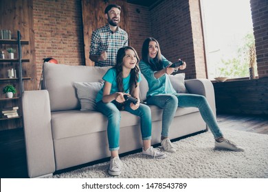 Portrait of excited people and little girl with brunet hair play videogame wearing denim jeans t-shirt sit divan in house indoors