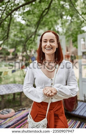 portrait of excited redhead woman in boho outfit looking at camera outdoors in retreat center