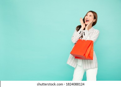 Portrait Of Excited Screaming Young Asian Woman Holding Shopping Bag Isolated Over Green Background, Wow And Surprised Concept