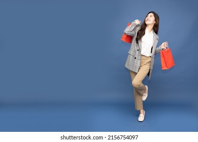 Portrait Of Excited Screaming Young Asian Woman Holding Shopping Bag Isolated Over Blue Background, Wow And Surprised Concept, Full Body Composition