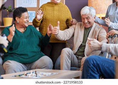 Portrait of excited senior man playing board game with multiethnic group of friends at retirement home - Powered by Shutterstock