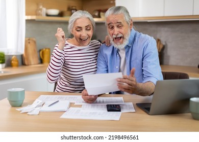 Portrait Of Excited Senior Spouses With Papers Celebrating Good News In Kitchen, Happy Elderly Couple Reading Mail And Enjoying Success, Emotionally Reacting To Credit Approvance Or Financial Profit