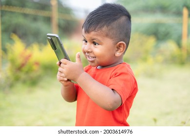 Portrait Of Excited Surprised Indian Chubby Kid Laughing By Looking Into Mobile Phone - Concept Of Children Mobile Addiciton, Internet And Technology
