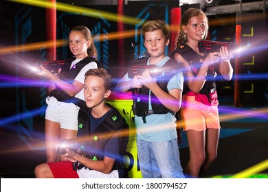Portrait of excited teen kids with laser guns during lasertag game in dark room..