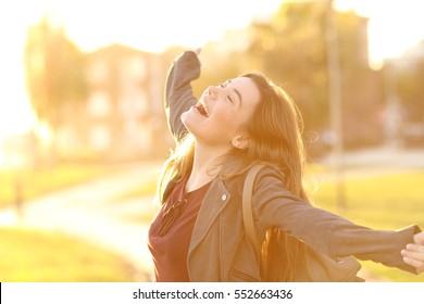 Portrait of an excited teenager girl raising arms and laughing in the street at sunset with a warm light in the background - Powered by Shutterstock