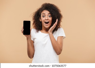 Portrait of an excited young african woman showing blank screen mobile phone isolated over beige background