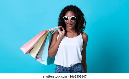 Portrait Of An Excited Young African Woman Hand Holding Shopping Bag Isolated Over Blue Background.