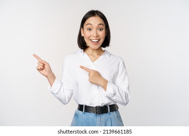 Portrait of excited young asian woman, office lady pointing fingers left at discount, showing sale banner, standing over white background - Powered by Shutterstock